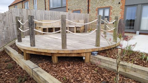 Circular timber deck with rope and post balustrade outside a flint cottage