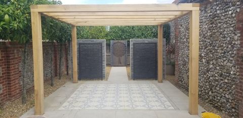 Timber pergola framing decorative screens and a patterned tiled path in a flint-walled garden